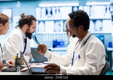 Diversi medici si uniscono in una riunione per discutere dei servizi di trattamento nel gabinetto. Medici autorizzati che esaminano i risultati dei raggi X e le cartelle cliniche per sviluppare piani di trattamento efficaci e competenze. Foto Stock