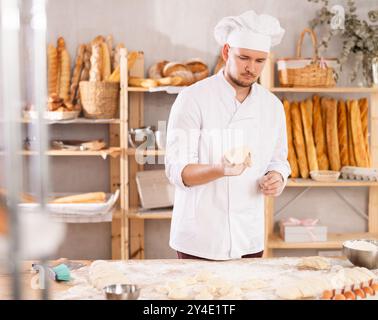 il fornaio professionista si trova al banco di lavoro, impastando e modellando l'impasto per preparare pane e baguette Foto Stock