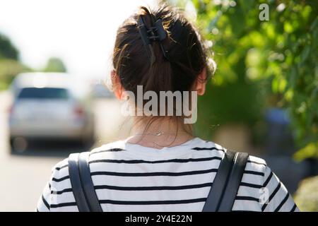 Una ragazza solitaria con i capelli puntati e uno zaino cammina con le spalle alla macchina fotografica lungo il marciapiede di una città europea in estate. Viaggia da solo c Foto Stock