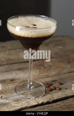 Bicchiere di deliziosi martini espresso e chicchi di caffè su un tavolo di legno, primo piano Foto Stock