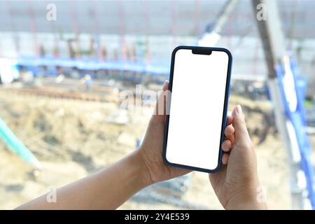 Primo piano di mani che tengono lo smartphone con schermo vuoto sul cantiere sullo sfondo Foto Stock