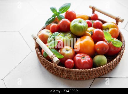 Un'abbondante collezione di pomodori colorati riempie un cesto intrecciato, caratterizzato da varie dimensioni e sfumature che si appoggiano su un ripiano della cucina a fine estate Foto Stock