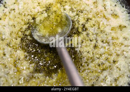 Golden Ghee bolle furiosamente in una padella, un cucchiaio di metallo appoggiato sulla superficie. Foto Stock