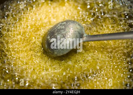 Le bollicine dorate ballano nella calda Ghee, un cucchiaio intempato sul bordo che suggerisce le creazioni culinarie. Foto Stock