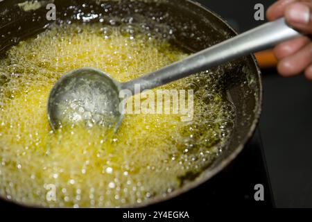 Le bollicine dorate sorgono nel Ghee caldo mentre lo chef controlla la temperatura di cottura, pronto per la frittura. Foto Stock