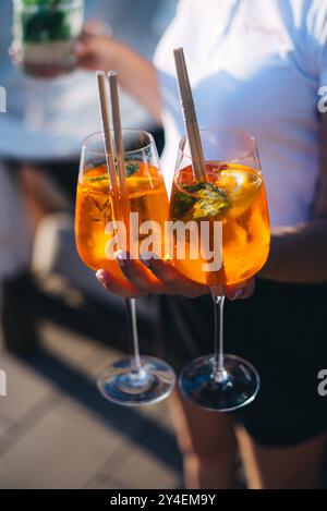 Cocktail luminoso e colorato aperol spritz in mano da cameriere in un guanto sullo sfondo. Foto Stock