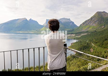 I bambini, in piedi sul bordo di una piattaforma panoramica lunga 44 metri, si affacciano sull'acqua del Bergsfjord, godendosi la vista sull'isola di Senja, nord nord nord Foto Stock