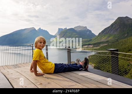 I bambini, in piedi sul bordo di una piattaforma panoramica lunga 44 metri, si affacciano sull'acqua del Bergsfjord, godendosi la vista sull'isola di Senja, nord nord nord Foto Stock