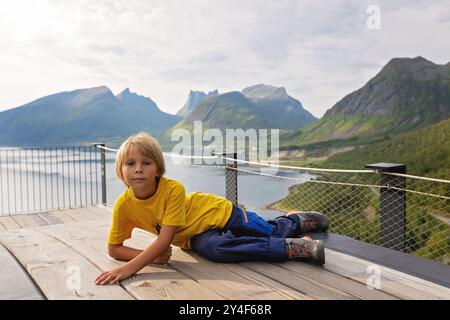 I bambini, in piedi sul bordo di una piattaforma panoramica lunga 44 metri, si affacciano sull'acqua del Bergsfjord, godendosi la vista sull'isola di Senja, nord nord nord Foto Stock