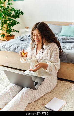 Una giovane e bella donna di grandi dimensioni si rilassa a casa sorseggiando un tè mentre si concentra sul suo laptop. Foto Stock