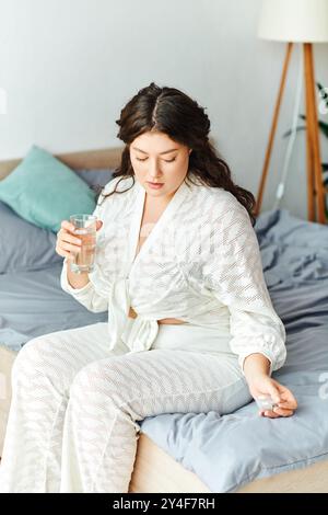 Una giovane e bella donna di grandi dimensioni si rilassa a casa, sorseggiando un bicchiere d'acqua mentre si riflette. Foto Stock