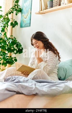 Una giovane donna più grande si rilassa sul suo letto, profondamente impegnata a leggere un libro nella sua accogliente camera. Foto Stock