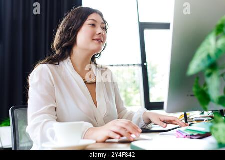 La luce solare intensa riempie l'accogliente ufficio mentre una donna di grandi dimensioni si impegna nel suo lavoro, sorridendo. Foto Stock