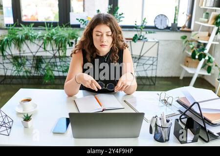 Una giovane donna d'affari con i capelli ricci si concentra intensamente sul suo laptop mentre organizza appunti alla sua scrivania. Foto Stock