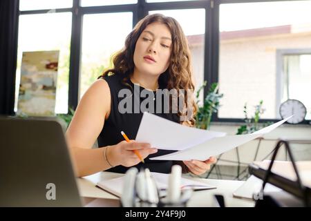 Una giovane professionista di grandi dimensioni siede alla sua scrivania, rivede i documenti e si immerge nel lavoro in un'atmosfera d'ufficio stimolante. Foto Stock