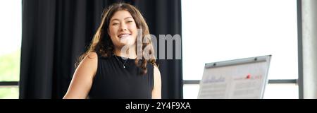 Una giovane donna sicura di sé con lunghi capelli ricci coinvolge con entusiasmo i colleghi in un ambiente luminoso da ufficio. Foto Stock