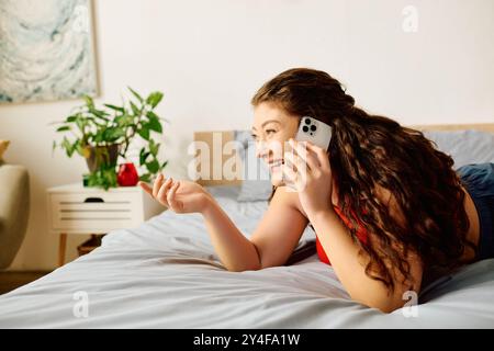 Una donna allegra e di grandi dimensioni con capelli ricci si gode una vivace conversazione a casa nella sua invitante camera da letto. Foto Stock