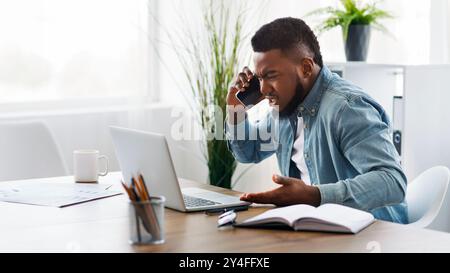 Imprenditore deluso parlando al telefono e guardando il laptop con rabbia Foto Stock