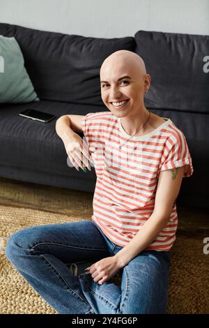 Una donna allegra e calva siede comodamente sul pavimento, mostrando il suo spirito sicuro di sé. Foto Stock