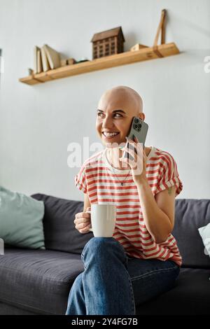 Una giovane donna calva sorride brillantemente mentre si impegna in una vivace conversazione telefonica sorseggiando un tè. Foto Stock