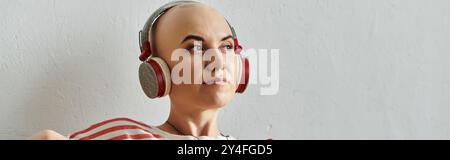 Una bella donna calva ama la musica con le cuffie, abbracciando la sua bellezza e il suo stile unici. Foto Stock