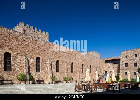 Questo storico castello trasformato in hotel presenta una splendida architettura su un cielo azzurro e cristallino, invitando gli ospiti a godersi il suo incantevole cortile. Foto Stock