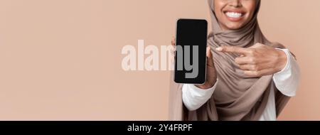 Unirriconoscibile Afro Woman In Hijab Che Punta Allo Smartphone Con Schermo Nero Foto Stock