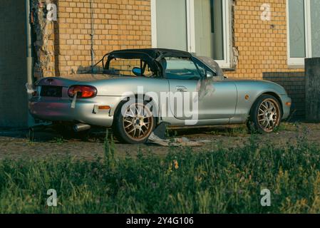 Un'auto abbandonata semplicemente parcheggiata in un ambiente industriale, rottami, arrugginita, vandalismo Foto Stock