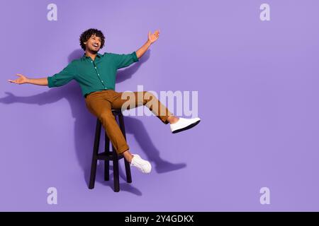 Foto a tutta lunghezza del corpo di un bellissimo ispanico al bar che si rilassa su una sedia a sdraio, braccia rialzate e rilassate isolate su sfondo di colore viola Foto Stock