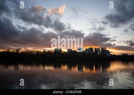Rosslyn Skyline Sunset Potomac River Arlington Stati Uniti // ARLINGTON, Stati Uniti — lo skyline di Rosslyn, Virginia, si staglia contro un tramonto sul fiume Potomac. Le nuvole punteggiano il cielo mentre un bagliore dorato illumina l'orizzonte, creando uno sfondo drammatico per il paesaggio urbano di fronte a Washington DC. Foto Stock