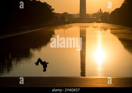 WASHINGTON DC, Stati Uniti: Il monumento a Washington, la cupola del Campidoglio e la piscina riflettente viste dal Lincoln Memorial all'alba durante l'equinozio primaverile e autunnale. Il sole sorge perfettamente in linea con il National Mall, proiettando un caldo bagliore sui monumenti storici più rappresentativi. In questo scatto, una persona viene sagomata facendo un backflip vicino alla linea di galleggiamento. Foto Stock