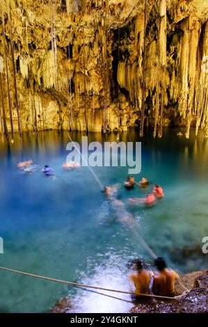 VALLADOLID, Messico: I nuotatori si rinfrescano nelle acque azzurre del Cenote Xkakah, noto anche come Cenote Dzitnup, vicino a Valladolid, nella penisola dello Yucatan in Messico. Questa piscina naturale sotterranea, formata dal crollo della roccia calcarea, offre ai visitatori un rifugio rinfrescante nelle sue acque cristalline. Foto Stock