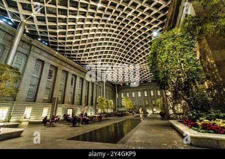 WASHINGTON DC - il Robert and Arlene Kogod Courtyard dello Smithsonian's Donald W. Reynolds Center for American Art and Portraiture, illuminato di notte con il cielo scuro visibile attraverso il suo caratteristico soffitto di vetro. Progettato da Foster + Partners e completato nel 2007, questo 28 cortile coperto di 000 metri quadrati collega lo Smithsonian American Art Museum e la National Portrait Gallery. L'elegante spazio interno presenta una tettoia di vetro ondulata e funge da popolare area di ritrovo pubblico nel centro di Washington, DC. Foto Stock