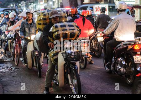 HANOI, Vietnam: Scooter e biciclette affollano una stradina nel centro storico di Hanoi durante la serata. La vivace scena mostra la caotica ma vibrante vita di strada tipica di Hanoi, mentre la gente del posto percorre le strade trafficate in moto e in bicicletta. Foto Stock