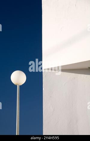 Un lampione rotondo si trova accanto a una luminosa parete imbiancata sotto un cielo azzurro, che mostra una calda giornata a Siviglia. Foto Stock