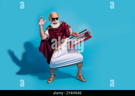 Foto di un uomo gioioso positivo in abiti antichi greci dio ballare divertirsi isolato su sfondo di colore blu Foto Stock