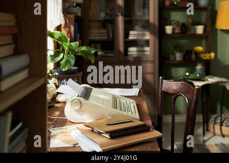 Configurazione vintage per home Office con una vecchia macchina da scrivere, scrivania in legno, varie piante d'casa, libri e quaderni. Luce solare che illumina la stanza attraverso tende parzialmente aperte Foto Stock