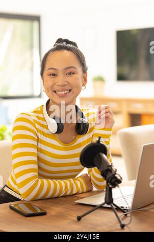 Donna sorridente con cuffie che registrano podcast utilizzando laptop e microfono Foto Stock