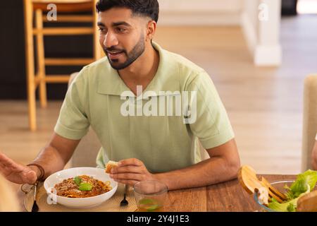 Mangiare pasta e parlare, l'uomo si diverte a tavola con diversi amici Foto Stock