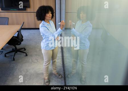 Scrivendo su una lavagna di vetro, una donna d'affari che fa brainstorming idee in un ufficio moderno Foto Stock