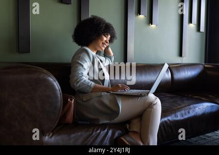 Lavora su un computer portatile, donna d'affari seduta su un divano in pelle in un ufficio moderno Foto Stock