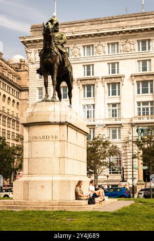 Un paio di persone che leggevano libri sedevano sui gradini sotto la statua di Edoardo VII al molo Albert di Liverpool Foto Stock