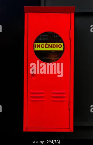 Scatola estintore brasiliana dipinta di rosso brillante con una porta con una finestra e l'iscrizione INCÊNDIO scritta in portoghese. Foto Stock