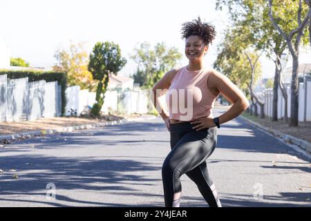 Donna sorridente con capelli ricci che si allungano in strada, indossano smartwatch e spazio per copiare Foto Stock