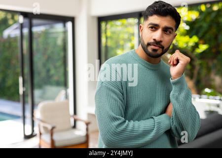 Pensando profondamente, un uomo indiano in maglione verde in piedi all'interno vicino a grandi finestre Foto Stock