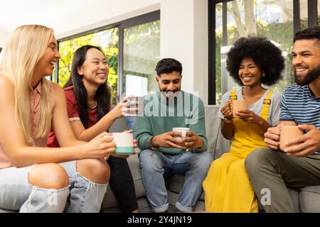 Giovani amici seduti sul divano, bevendo un caffè e ridendo insieme in casa Foto Stock