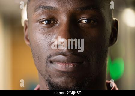 Primo piano di un uomo afroamericano che guarda con fiducia la fotocamera in ambienti professionali Foto Stock