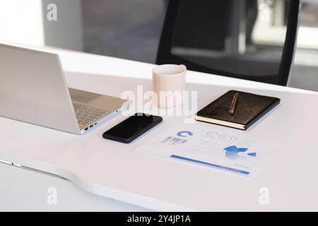 Laptop, smartphone, notebook e tazza di caffè su una moderna scrivania da ufficio Foto Stock