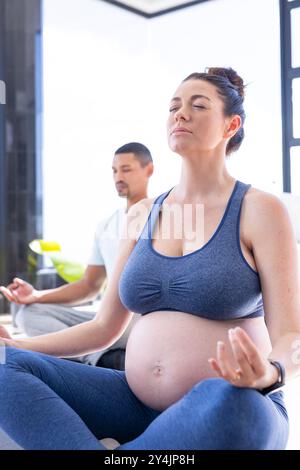 A casa, coppia multirazziale, donna incinta che medita con la partner, pratica yoga prenatale Foto Stock