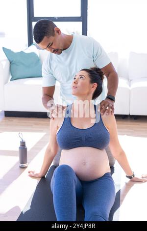 Coppia multirazziale, donna incinta che si allunga sul tappetino da yoga con partner che assiste a casa Foto Stock